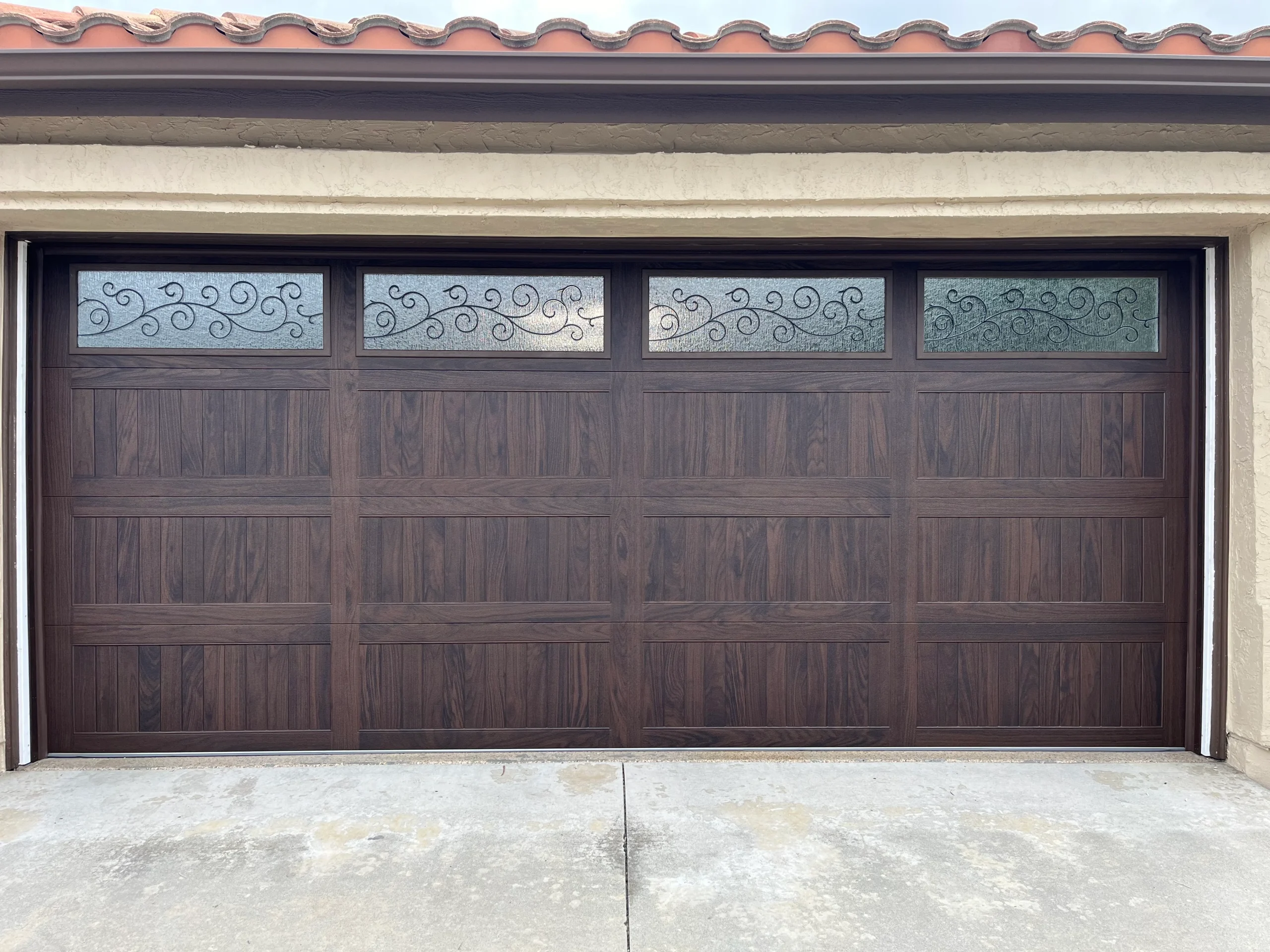 An elegant dark wood grain sectional door with decorative wrought-iron style window inserts, installed by a professional garage door company in San Diego.