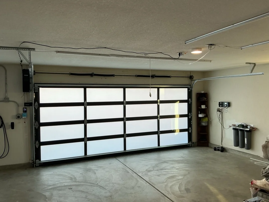An interior view of a contemporary glass and black aluminum frame garage door, showcasing the overhead spring and tracking system to help illustrate how can garage door repair problems be identified.