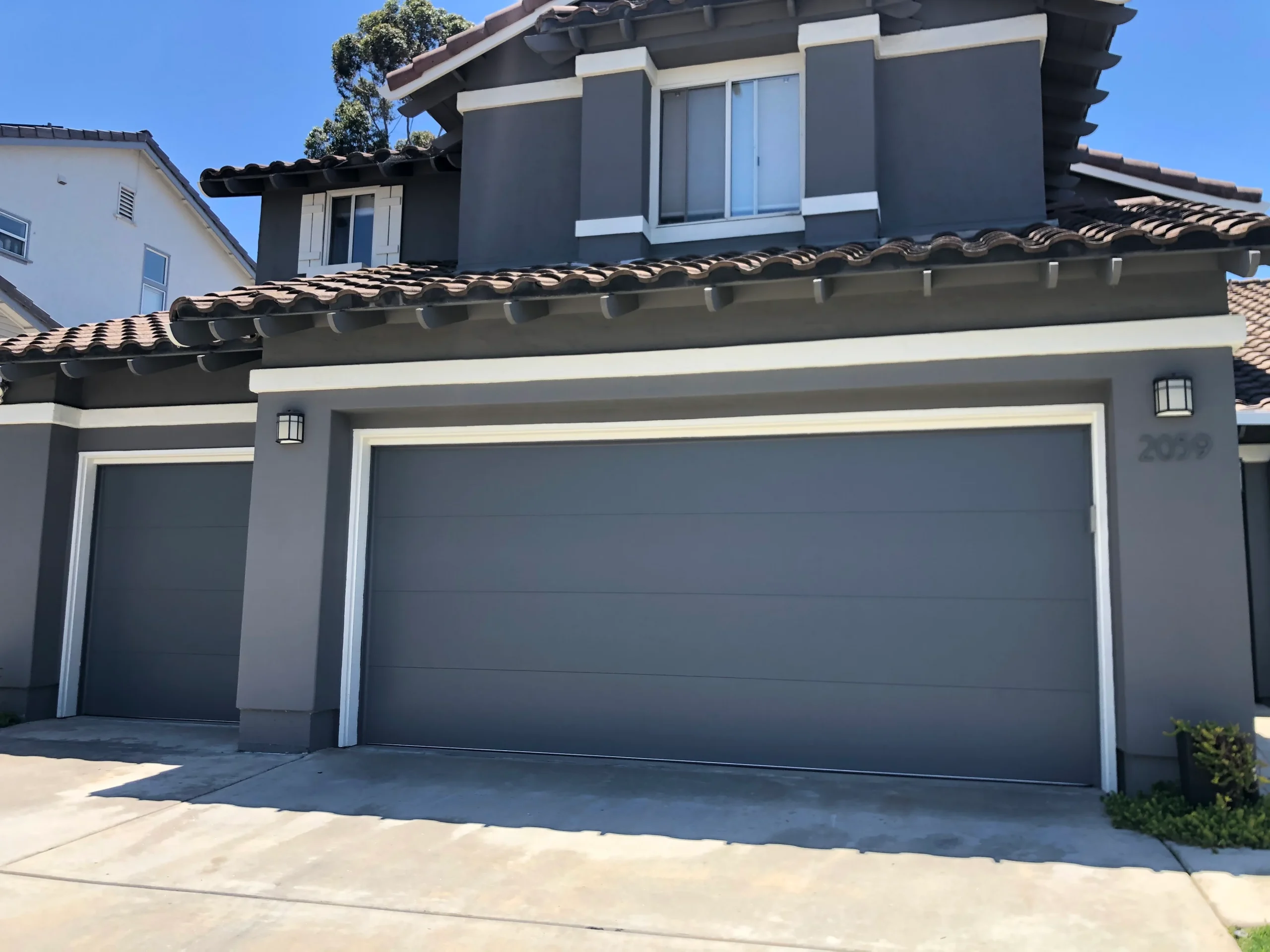 An exterior view of a modern two-story gray house with matching gray flush-panel garage doors, perfect for showcasing what is included in garage door repair services.
