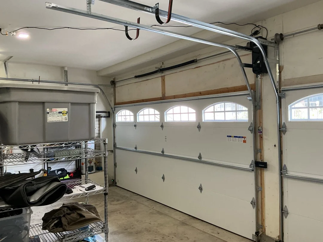 An interior garage view of a white sectional door with arched window inserts and a wall-mounted opener, highlighting components to evaluate when your garage door needs attention.