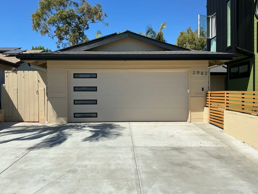 A modern beige residential garage with a flush panel door and vertically aligned tinted windows, perfect for a routine garage door inspection.
