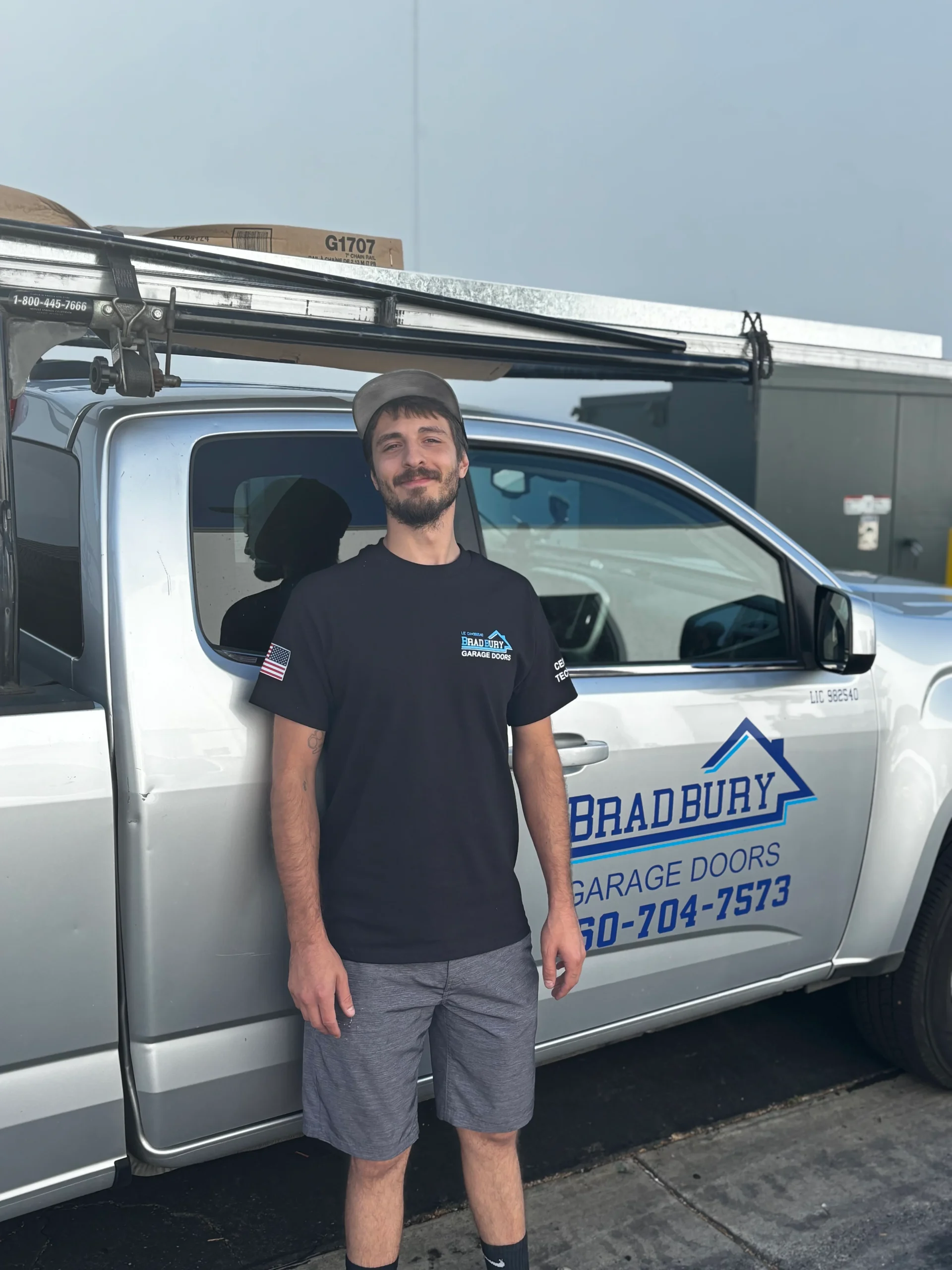 A service technician from Bradbury Garage Doors standing in front of a silver company truck, ready to complete a professional garage door safety check.