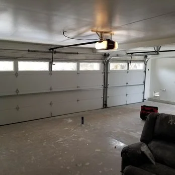 A ceiling-mounted unit with an integrated light fixture operating a closed white sectional door, featuring a LiftMaster Garage Door Opener.
