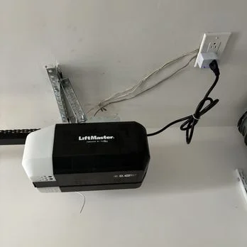 A ceiling-mounted motor unit plugged into a nearby wall outlet during a LiftMaster garage door opener installation.