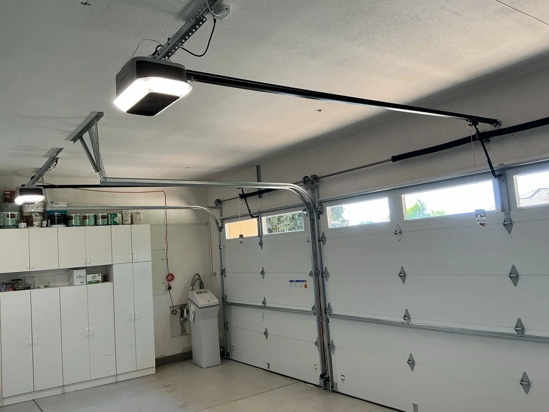 An interior view of a well-lit garage with white sectional doors and automatic openers, perfect for a summer maintenance guide for your liftmaster garage door.