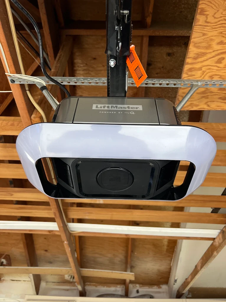 A close-up view of an overhead motor unit mounted to wooden ceiling framing, showing a well-maintained LiftMaster garage door.