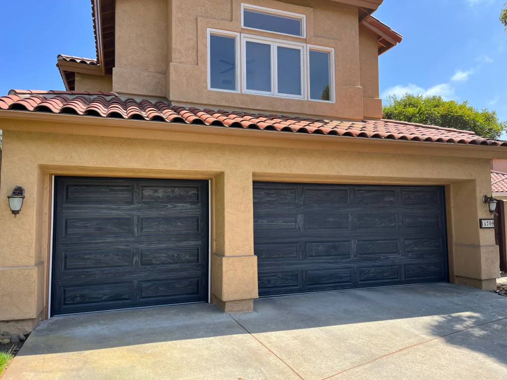 A beautiful stucco home featuring dark wood-grain patterned overlay doors, highlighting high-quality garage door materials.