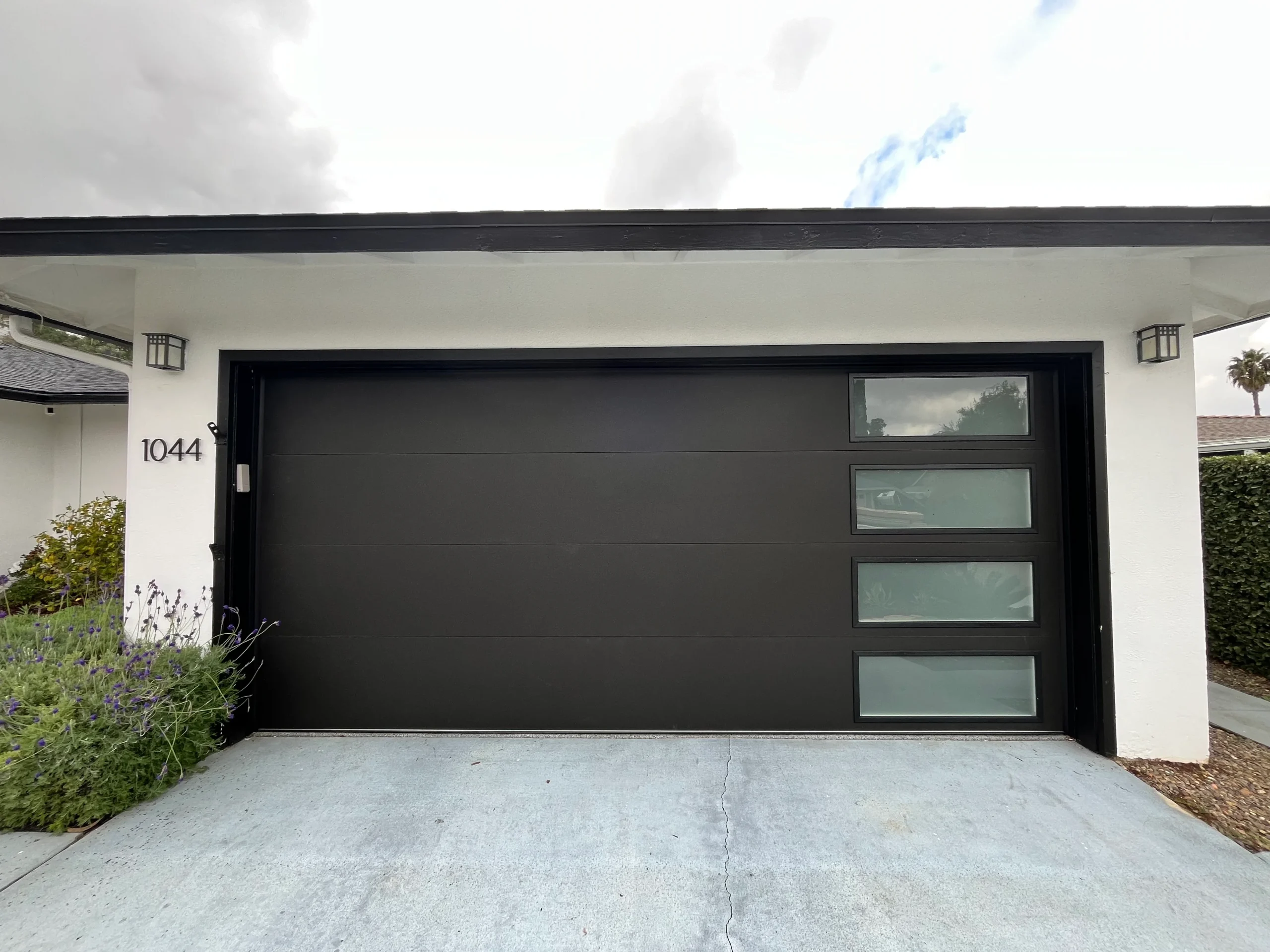 A sleek, modern matte black garage door with vertically stacked frosted glass window inserts on a white stucco home, highlighting options for garage door repair or replacement