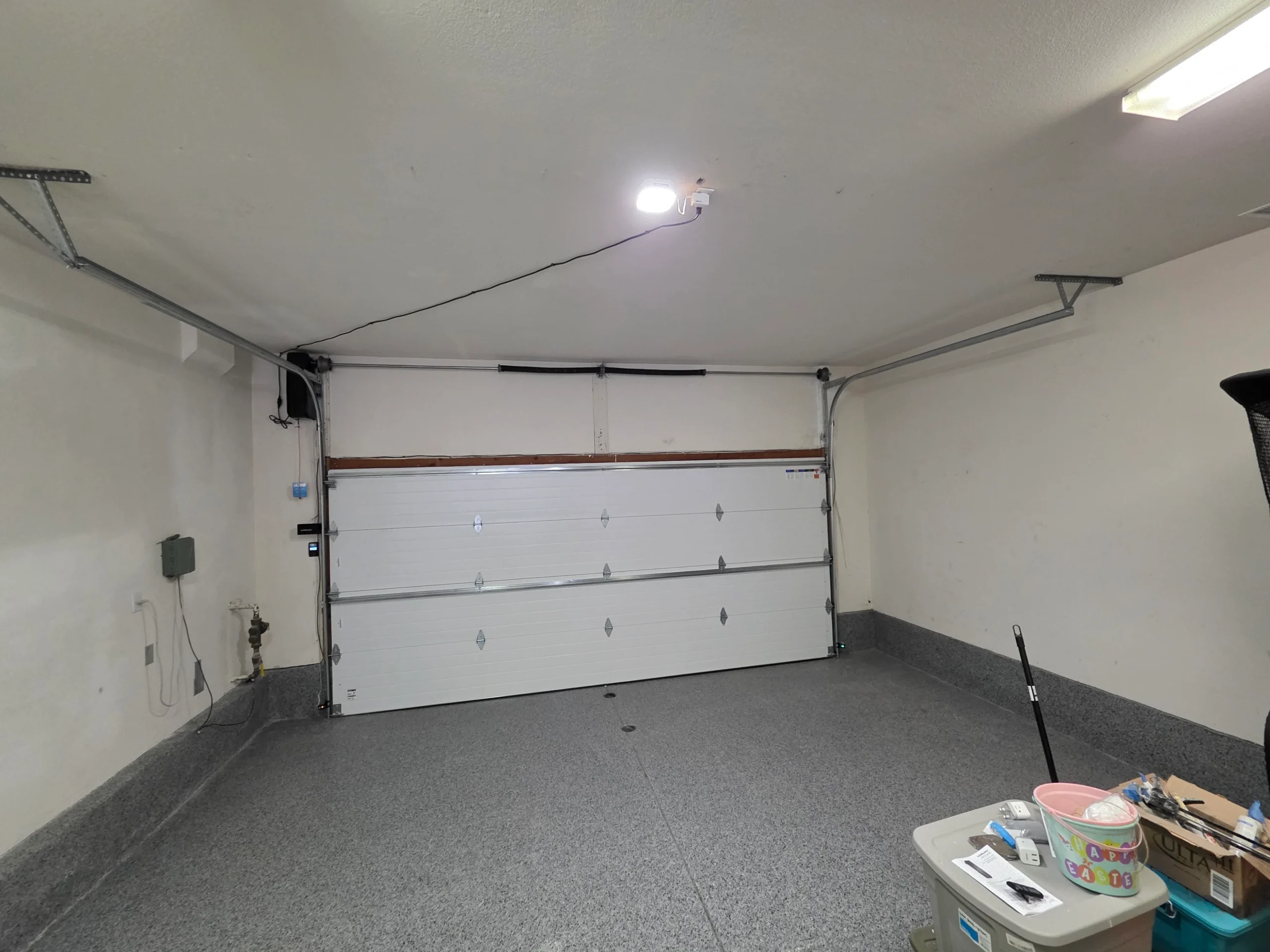 An interior view of a spacious garage with an epoxy floor, featuring a newly installed white sectional system after a professional garage door replacement.