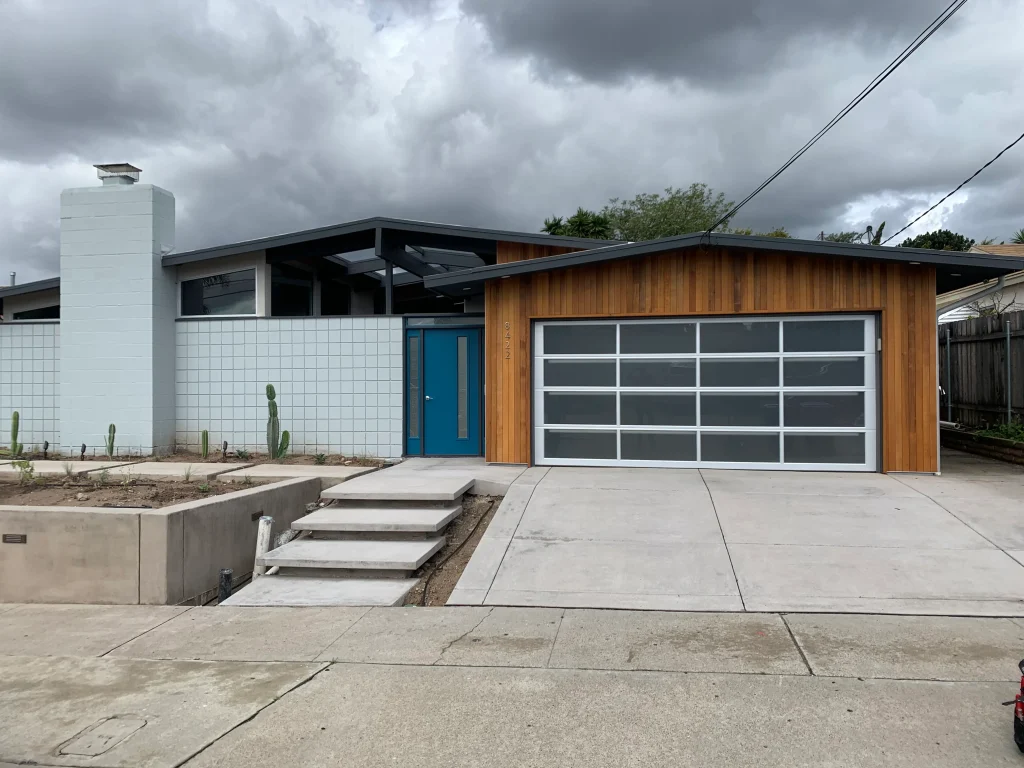 A mid-century modern home exterior featuring wood vertical siding and a full-view glass garage door style.