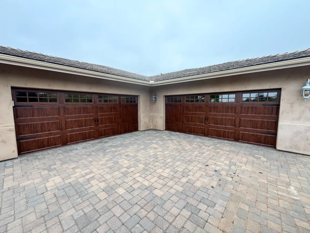 A spacious paved driveway facing two custom dark wood carriage-style doors, ideal for tips on summer garage door maintenance.