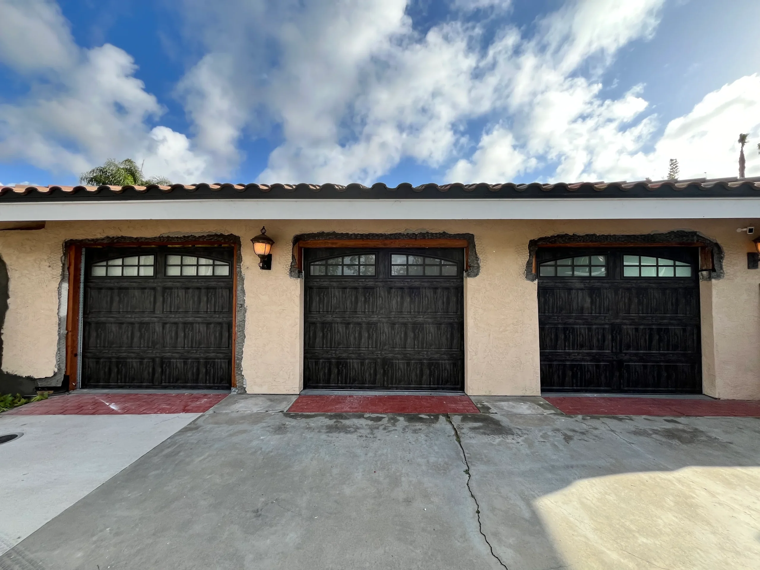 A three-car garage under construction showcasing elegant, dark wood-finish carriage style installations, comparing different types of garage doors.